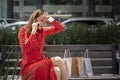 Young upset Caucasian woman in red dress sitting on a bench talking on the phone to clear up a charge on her credit card