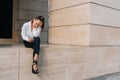 A young upset girl in black pants white shirt sits on a stone surface with a phone in her hands Royalty Free Stock Photo