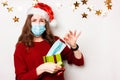 A young upset girl in a red sweater and a medical mask takes out a mask from a gift for the new year and christmas