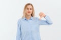 Young upset gloomy woman with fair-haired is frowning and showing thumb-down, gesture with hand, standing over white background in Royalty Free Stock Photo