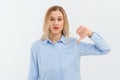 Young upset gloomy woman with fair-haired is frowning and showing thumb-down, gesture with hand, standing over white background in Royalty Free Stock Photo