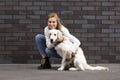 Young urban girl caresses a dog on the street against a wall, a woman walks a retriever puppy and hugs him Royalty Free Stock Photo