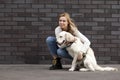 Young urban girl caresses a dog on the street against a wall, a woman walks a retriever puppy and hugs him Royalty Free Stock Photo