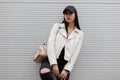 Young urban woman in a trendy white leather jacket in vintage ripped jeans in a stylish black baseball cap Royalty Free Stock Photo