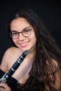 A brunette girl with her clarinet, with glasses, lying down laughing. on a black uniform background Royalty Free Stock Photo