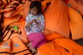 A young vietnamese girl sitting in a pile of orange life vests