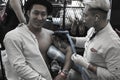 Young Vietnamese man smiles as he looks at the camera while he gets a tattoo on his left arm 