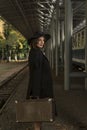 Young vintage lady with retro suitcase waiting train at railroad station. Portrait of middle-aged woman in coat and hat Royalty Free Stock Photo