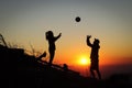 Young volleyball couple enjoying the top of a pink mountain with a ball at sunset. Silhouettes of a woman and a player pinching