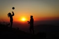 Young volleyball couple enjoying the top of a pink mountain with a ball at sunset. Silhouettes of a woman and a player pinching