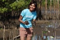 A young volunteer woman in blue t-shirt planting sapling tree in deep mud at mangrove forest for increasing mangrove cover world- Royalty Free Stock Photo