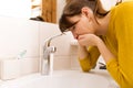 Young vomiting woman near sink in bathroom