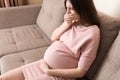 Young vomiting woman sitting on sofa and suffering with nausea. Pregnancy expectation concept, copy space