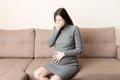 Young vomiting woman sitting on sofa and suffering with nausea. Pregnancy expectation concept, copy space Royalty Free Stock Photo