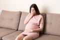 Young vomiting woman sitting on sofa and suffering with nausea. Pregnancy expectation concept, copy space