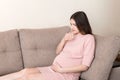 Young vomiting woman sitting on sofa and suffering with nausea. Pregnancy expectation concept, copy space