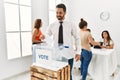 Young voter man smiling happy putting vote in voting box standing by ballot at electoral center Royalty Free Stock Photo