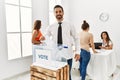 Young voter man smiling happy putting vote in voting box standing by ballot at electoral center Royalty Free Stock Photo