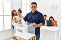 Young voter man smiling happy putting vote in voting box standing by ballot at electoral center Royalty Free Stock Photo