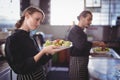 Young wait staff holding fresh salad plates while standing in commercial kitchen Royalty Free Stock Photo