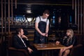 A young waiter guy opens a bottle of wine at the table in a restaurant Royalty Free Stock Photo