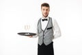 Young waiter in uniform holding tray with glasses of champagne while thoughtfully looking in camera over white Royalty Free Stock Photo