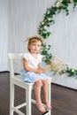 A young warm smiling girl is sitting on the wooden white chair.