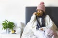 A young warmly dressed woman laying in bed with tea Royalty Free Stock Photo