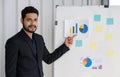 Young wavy hair, moustache and beard businessman in black suit  pointing finger at pie chart on white board. Training and Royalty Free Stock Photo