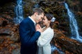 Young wedding couple softly holding hands. Breathtaking waterfall on background Royalty Free Stock Photo