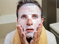 Young weird and funny man at home trying using beauty paper facial mask cleansing learning anti aging treatment in surprised face