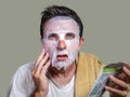 Young weird and funny man at home trying using paper facial mask cleansing applying anti aging facial treatment reading beauty Royalty Free Stock Photo