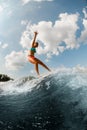young wet woman in colorful swimsuit masterfully balancing on wave on wakesurf board.
