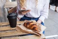 Young white blond woman having a break and holds smartphone in hand. Street veranda table in cafe with cardboard paper cup of Royalty Free Stock Photo