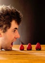 Young white boy with curly hair with his mouth open to eat strawberries.  Space for text on dark background Royalty Free Stock Photo