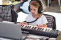 A young white Caucasian girl wearing headphones and playing a keyboard connected to a laptop personal computer