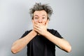 Young white caucasian unshaven guy with long gray hair close his mouth and silent on a gray background