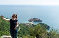 Young white girl making a selfie in the mountain and the adriatic sea in the background and Sveti Stefan.Woman with smart phone in