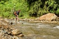 Young white man with backpack crosses the mountain river. Royalty Free Stock Photo