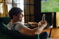 Young white man watching football match and drinking beer in front of the TV screen Royalty Free Stock Photo