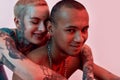 Young white pierced tattooed female with eyes closed hugging dark-skinned topless tattooed male from back , both smiling