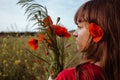 A young white teen girl portrait in profile stands with her back to camera with red blooming poppies flowers bouquet Royalty Free Stock Photo