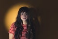 Young white woman with long dark hair standing in yellow spotlight looking at camera smiling holding vase with plant Royalty Free Stock Photo