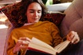 Young white woman reading book while lying on couch Royalty Free Stock Photo