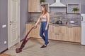 Young white maid is vacuuming floor in the kitchen