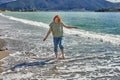 Young white woman walks barefoot on sand in surf line on beach in resort town of Fethiye in early spring.