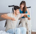 Young wife supporting husband on crutch after injury