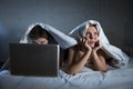 young wife upset unsatisfied and frustrated in bed while husband work on computer laptop ignoring her