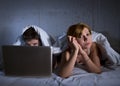 young wife upset unsatisfied and frustrated in bed while husband work on computer laptop ignoring her