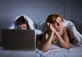 young wife upset unsatisfied and frustrated in bed while husband work on computer laptop ignoring her
